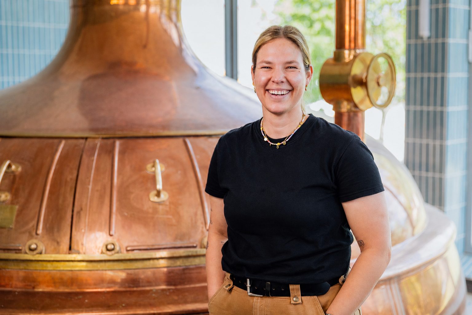 Laura lacht vor dem kupfernen Sudkessel der Brauerei