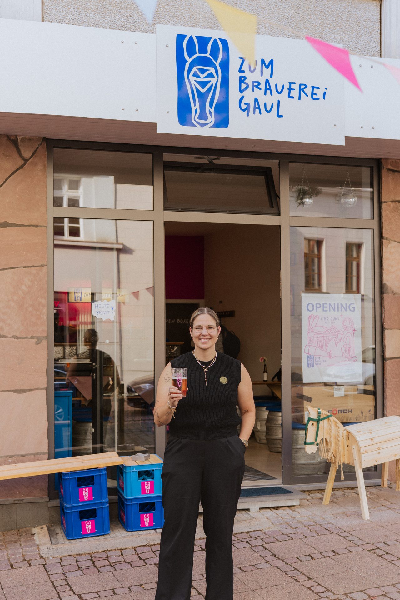 Laura mit Bier vor dem Eingang und dem Zum-Brauereigaul-Logo am Peterstor
